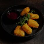Delicious crispy chicken nuggets served with a tangy dipping sauce on a black plate.