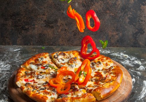 Side view pizza with slices of bell pepper and pizza slices and flour in board cookware on stone background